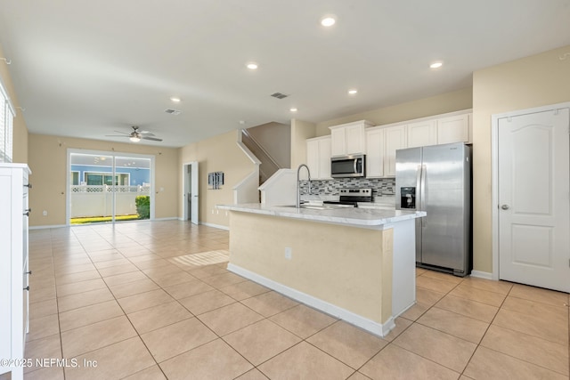 kitchen with backsplash, a center island with sink, ceiling fan, appliances with stainless steel finishes, and white cabinetry