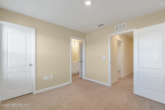 unfurnished bedroom featuring light carpet and ensuite bath