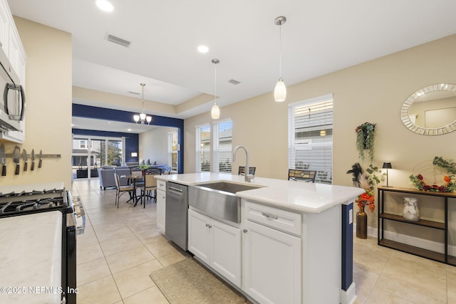 kitchen with appliances with stainless steel finishes, white cabinetry, sink, hanging light fixtures, and a kitchen island with sink