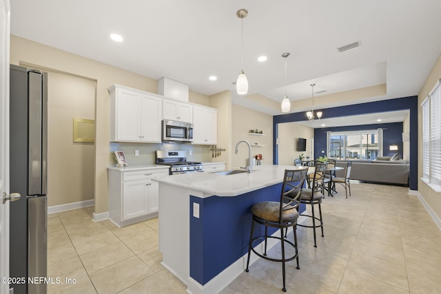 kitchen with sink, white cabinetry, pendant lighting, stainless steel appliances, and a kitchen island with sink