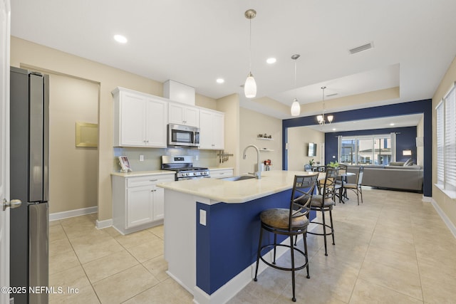 kitchen featuring decorative light fixtures, white cabinetry, sink, stainless steel appliances, and a center island with sink