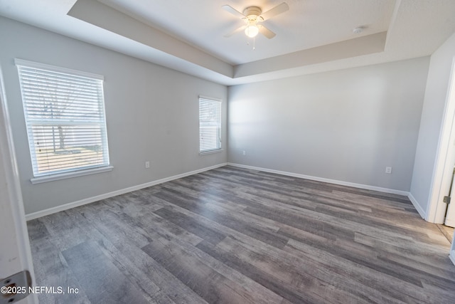 spare room with a raised ceiling, ceiling fan, and dark wood-type flooring