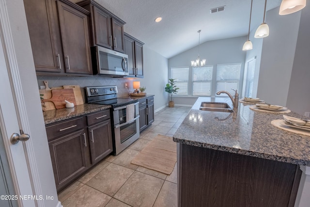 kitchen featuring dark stone counters, stainless steel appliances, vaulted ceiling, sink, and hanging light fixtures