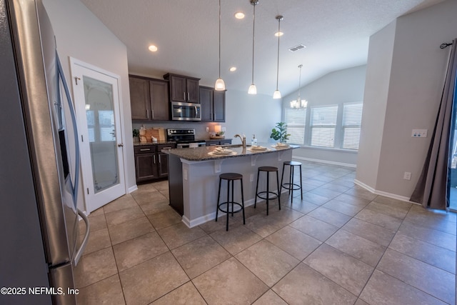 kitchen with dark stone counters, sink, vaulted ceiling, an island with sink, and appliances with stainless steel finishes