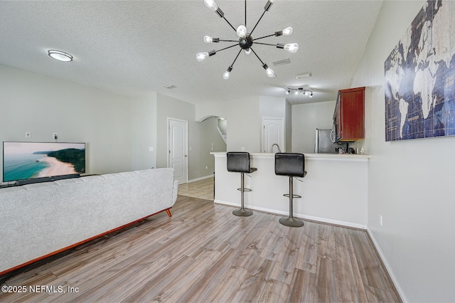 living room with an inviting chandelier, a textured ceiling, and light wood-type flooring