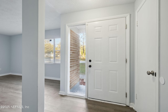 foyer entrance with a textured ceiling, baseboards, and wood finished floors