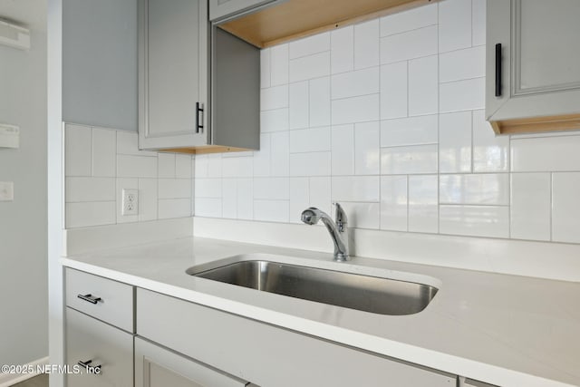 kitchen with tasteful backsplash, light countertops, a sink, and gray cabinetry