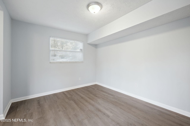 spare room with a textured ceiling, baseboards, and wood finished floors