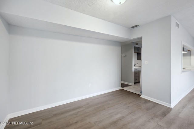 interior space with light wood-type flooring, baseboards, visible vents, and a textured ceiling