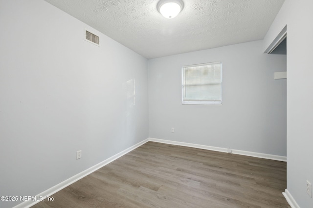 unfurnished room featuring a textured ceiling, wood finished floors, visible vents, and baseboards