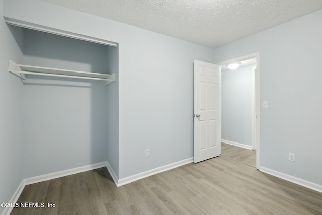 unfurnished bedroom featuring light wood-type flooring, baseboards, and a textured ceiling