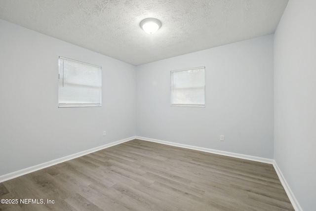 empty room featuring a textured ceiling, baseboards, and wood finished floors