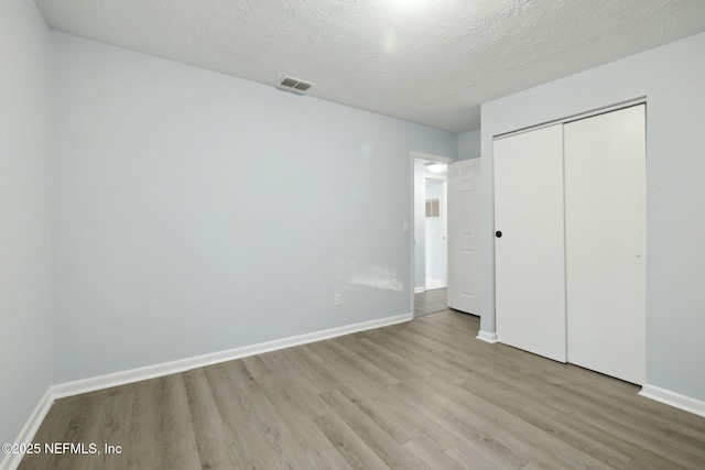 unfurnished bedroom with light wood-style floors, a closet, a textured ceiling, and baseboards