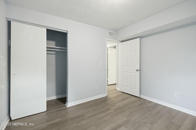 unfurnished bedroom with visible vents, a textured ceiling, baseboards, and wood finished floors