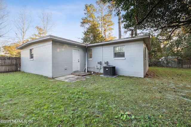 back of property featuring a lawn, fence, concrete block siding, and cooling unit