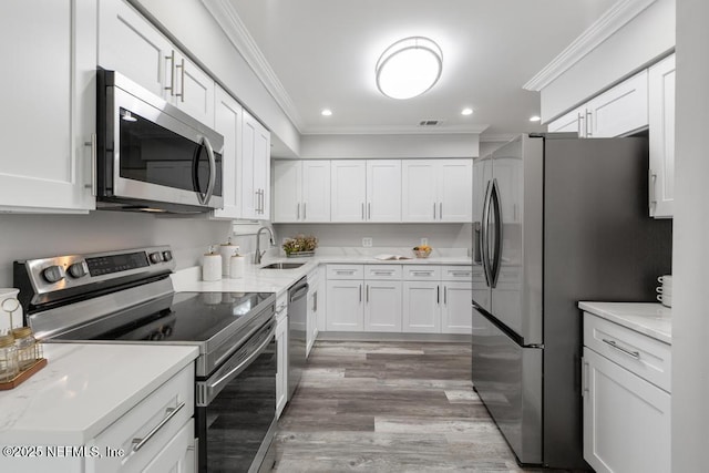 kitchen with white cabinets, appliances with stainless steel finishes, ornamental molding, and sink