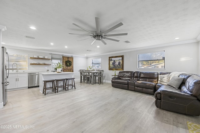 living room with ornamental molding, a textured ceiling, ceiling fan, sink, and light hardwood / wood-style flooring