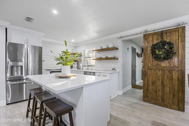 kitchen with stainless steel refrigerator with ice dispenser, a barn door, a center island, and white cabinetry