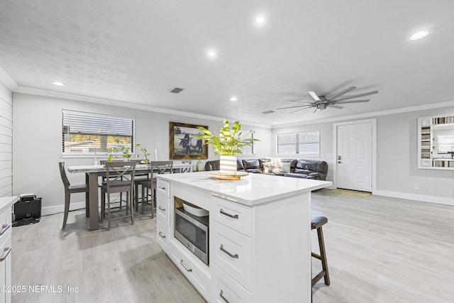 kitchen with stainless steel microwave, white cabinetry, crown molding, and a kitchen island