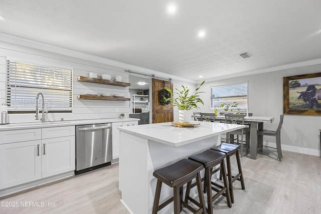 kitchen featuring a center island, sink, stainless steel dishwasher, a barn door, and white cabinetry