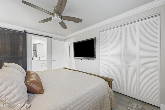 bedroom with ensuite bath, ceiling fan, a barn door, a closet, and ornamental molding