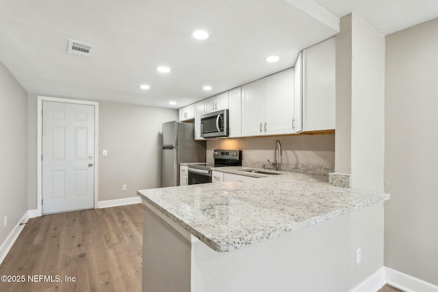 kitchen featuring white cabinetry, sink, stainless steel appliances, light stone counters, and kitchen peninsula