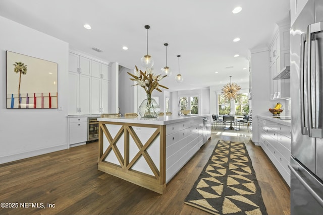 kitchen featuring hanging light fixtures, stainless steel fridge, white cabinets, and a large island with sink