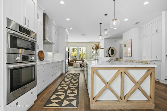 kitchen with white cabinets, hanging light fixtures, wall chimney exhaust hood, and appliances with stainless steel finishes