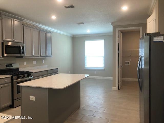 kitchen with gray cabinetry, a center island, stainless steel appliances, crown molding, and light wood-type flooring