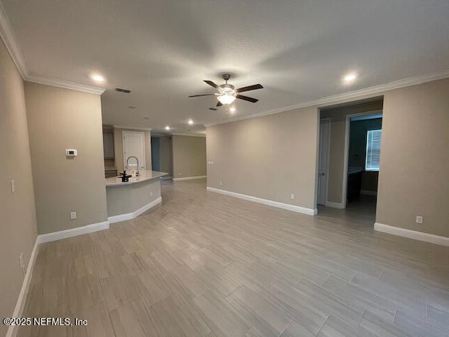 unfurnished living room featuring ceiling fan, sink, and crown molding