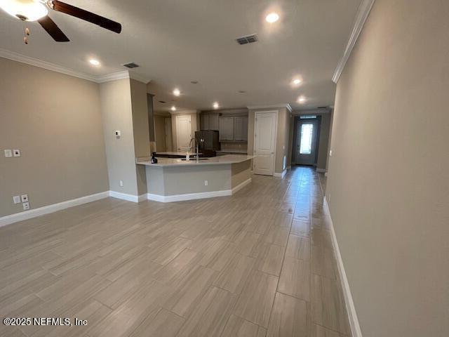 unfurnished living room featuring ceiling fan, crown molding, and sink