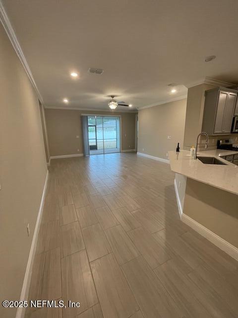 unfurnished living room with ceiling fan, crown molding, and sink