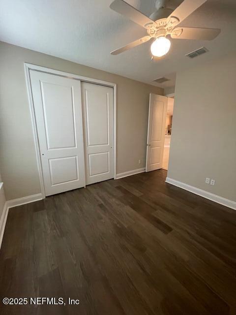 unfurnished bedroom with ceiling fan, dark hardwood / wood-style floors, and a closet