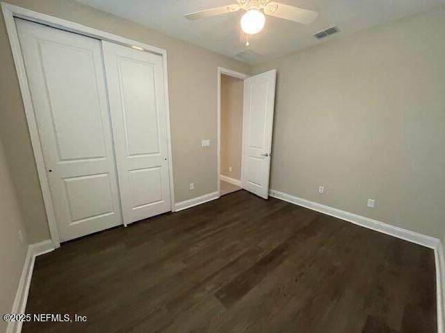 unfurnished bedroom with ceiling fan, dark hardwood / wood-style flooring, and a closet