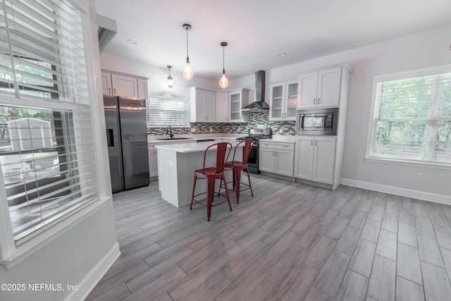 kitchen featuring a center island, wall chimney range hood, sink, hanging light fixtures, and stainless steel appliances