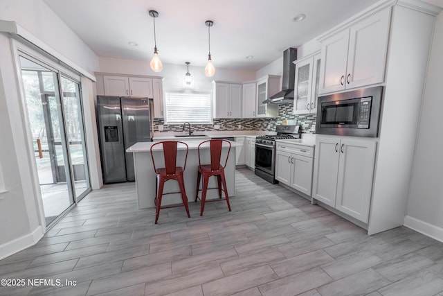 kitchen featuring wall chimney exhaust hood, stainless steel appliances, sink, decorative light fixtures, and a kitchen island