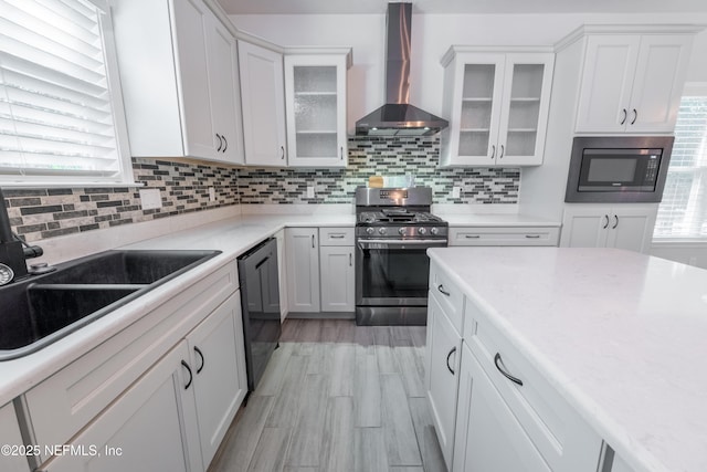 kitchen featuring black appliances, decorative backsplash, white cabinetry, and wall chimney range hood