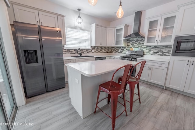 kitchen with appliances with stainless steel finishes, wall chimney exhaust hood, sink, decorative light fixtures, and a center island