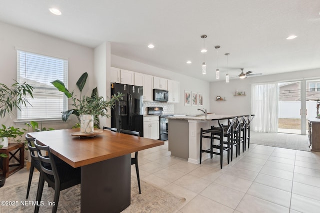 kitchen with a kitchen island with sink, black appliances, white cabinets, ceiling fan, and a kitchen bar