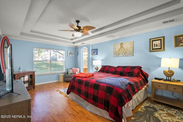 bedroom with hardwood / wood-style flooring, ensuite bath, ceiling fan, a textured ceiling, and a raised ceiling