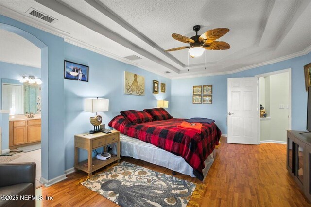 bedroom with ensuite bathroom, hardwood / wood-style floors, ceiling fan, a tray ceiling, and crown molding