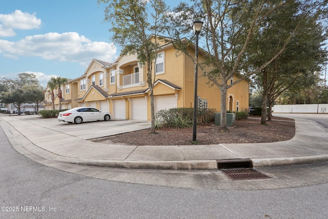 view of property featuring a balcony, a garage, concrete driveway, a residential view, and stucco siding