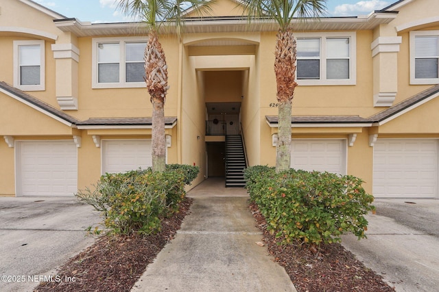 view of exterior entry with an attached garage, driveway, and stucco siding