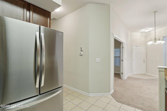 kitchen with light tile patterned floors, light colored carpet, visible vents, freestanding refrigerator, and an inviting chandelier