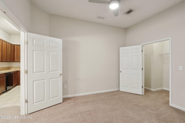 unfurnished bedroom with baseboards, a walk in closet, visible vents, and light colored carpet