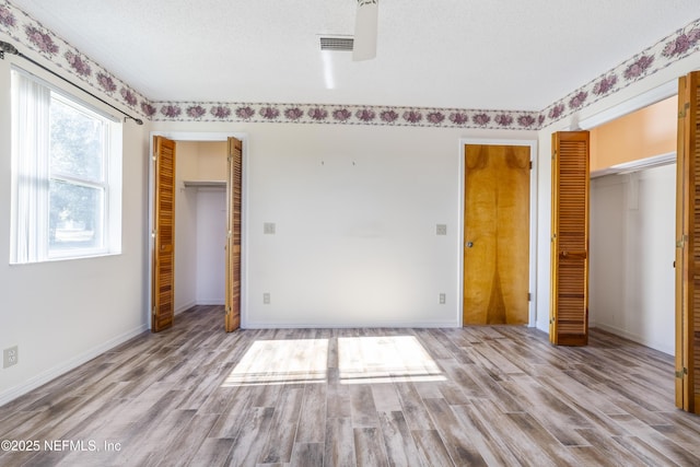 unfurnished bedroom with two closets, multiple windows, a textured ceiling, and light hardwood / wood-style flooring