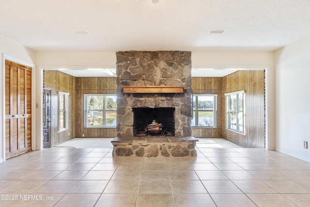 tiled living room with a textured ceiling, wooden walls, and a fireplace