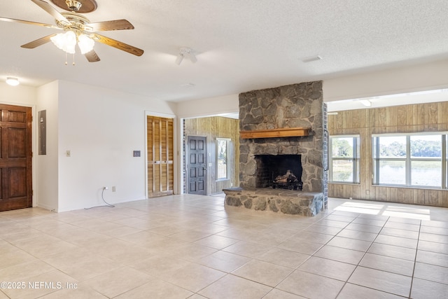 unfurnished living room featuring wooden walls, ceiling fan, light tile patterned floors, and a stone fireplace