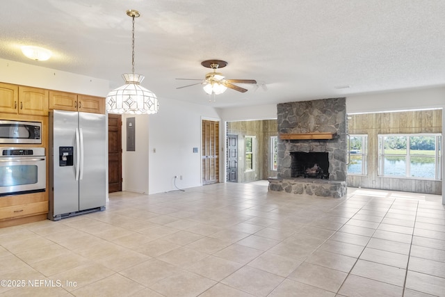 kitchen with hanging light fixtures, ceiling fan, appliances with stainless steel finishes, light tile patterned flooring, and a stone fireplace