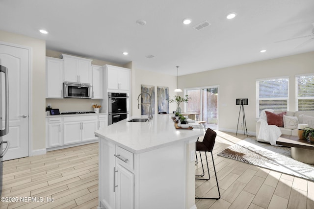 kitchen with stainless steel appliances, white cabinetry, a center island with sink, and sink